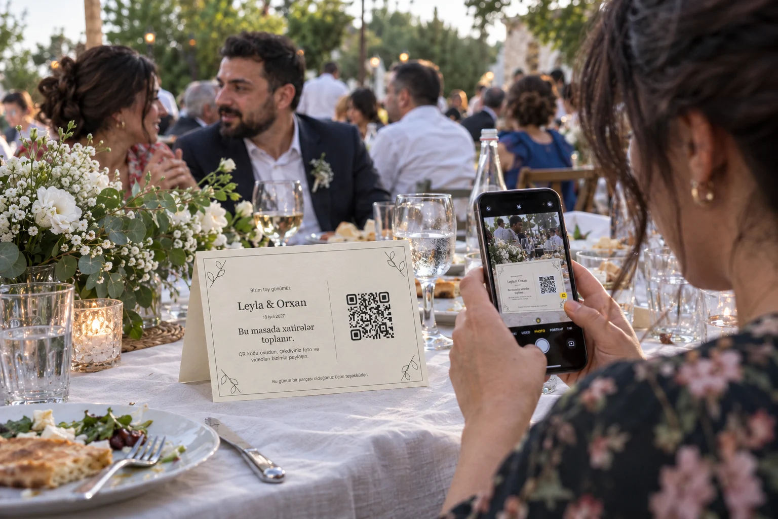 A guest scans Leyla and Orxan's botanical QR card at a garden wedding; a landscape table card folded from A4
