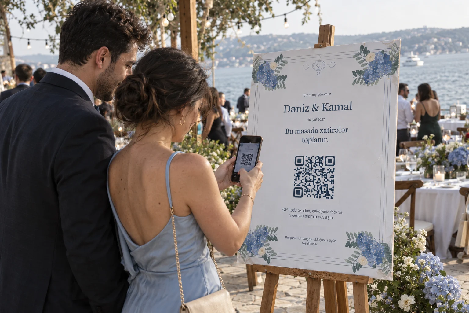 Guests scan Dəniz and Kamal's 50 × 70 cm QR welcome board with blue hydrangeas at a seaside wedding